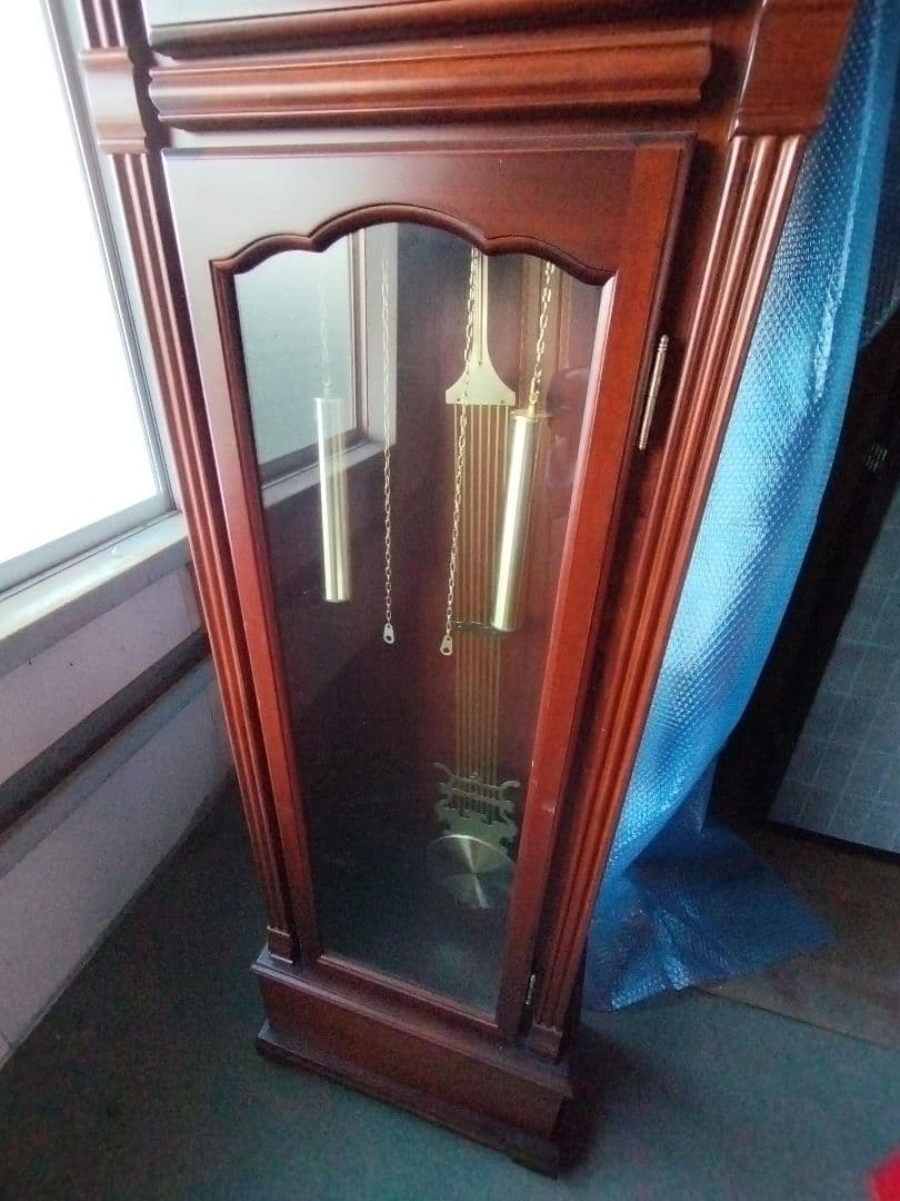 装飾的な文字盤と振り子を持つダークウッドの柱時計