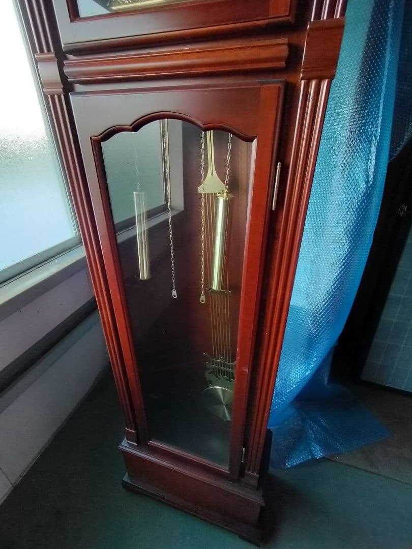 装飾的な文字盤と振り子を持つダークウッドの柱時計